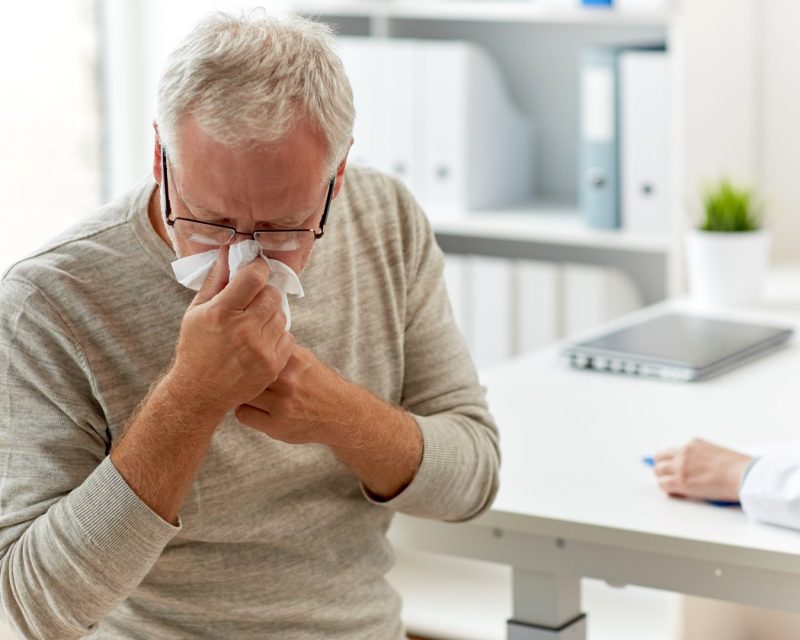 senior man blowing nose with napkin at hospital
